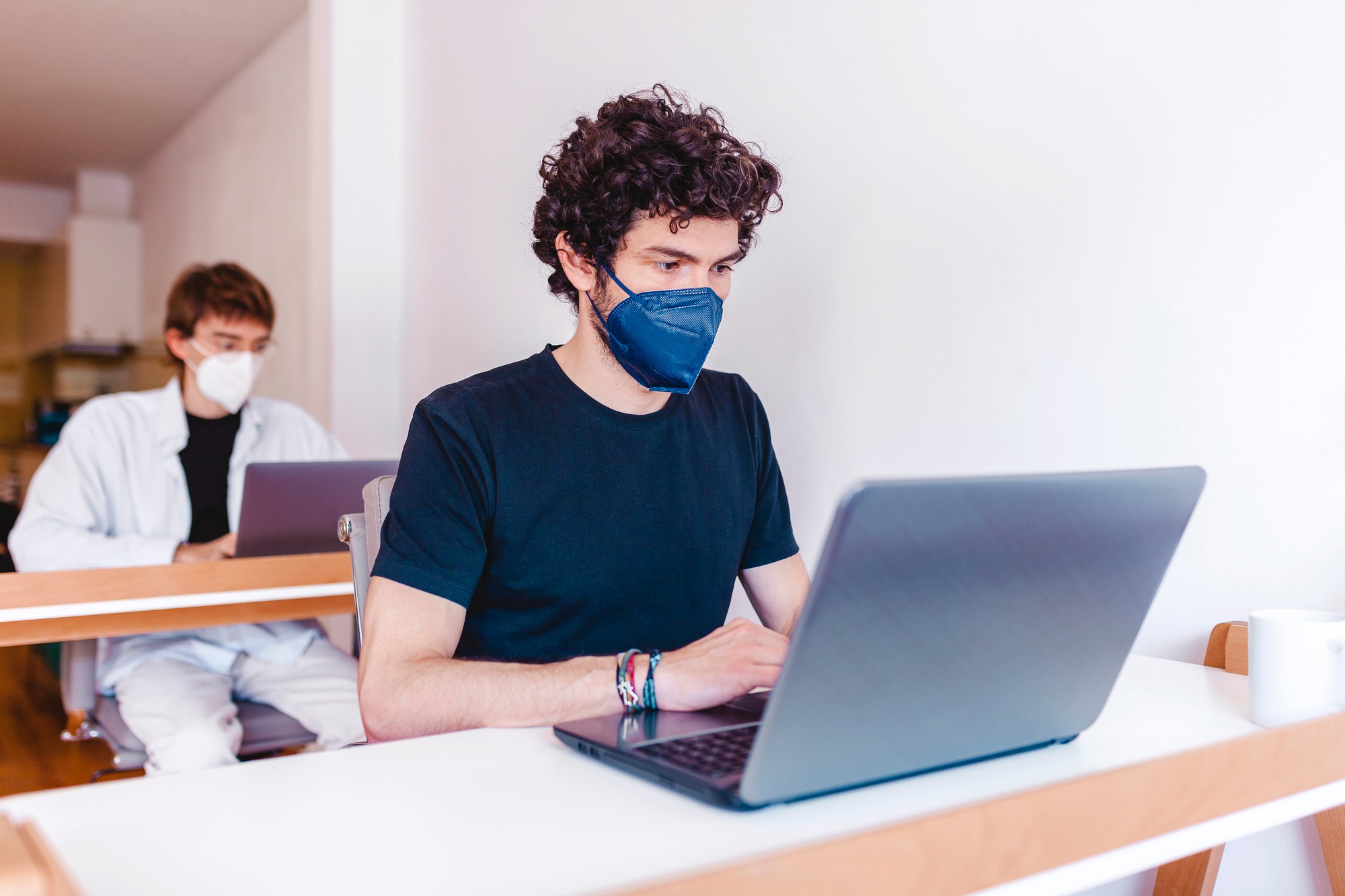 Two men wearing protective masks working on their laptop at office